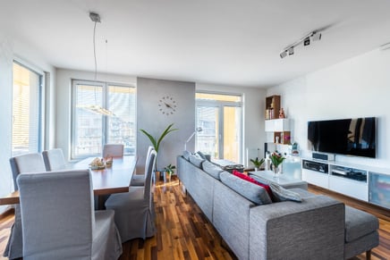Moderní obývací pokoj s jídelnou šedá sedačka dřevěný stůl.